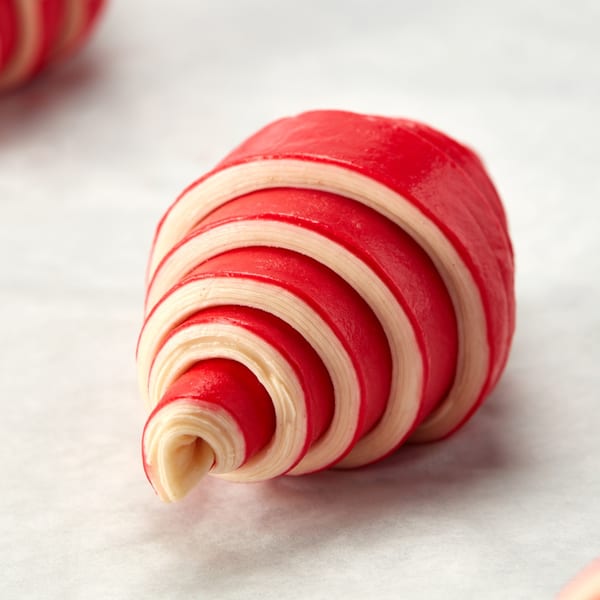 Unbaked red and white striped croissant dough, spiraled on a white surface at Bachour bakery.