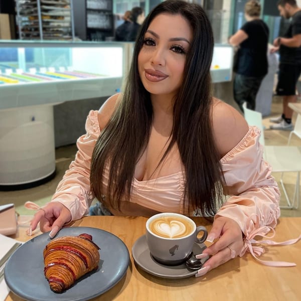 A woman at Bachour bakery with a croissant and a latte with heart-shaped foam.