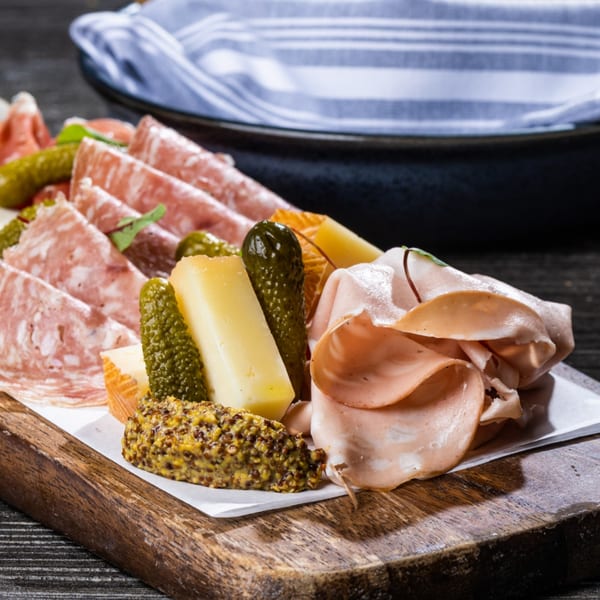Charcuterie board with sliced meats, cheese, pickles, and whole grain mustard on a wooden board.