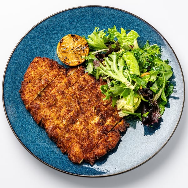Crispy breaded chicken schnitzel with a side salad and grilled lemon on a blue plate.