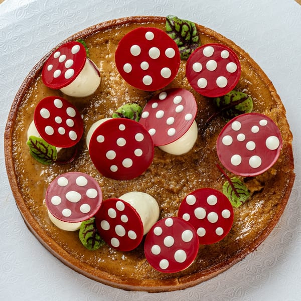 Bachour's mushroom-decorated tart features red and white chocolate fungi and green leaves on a brown base.