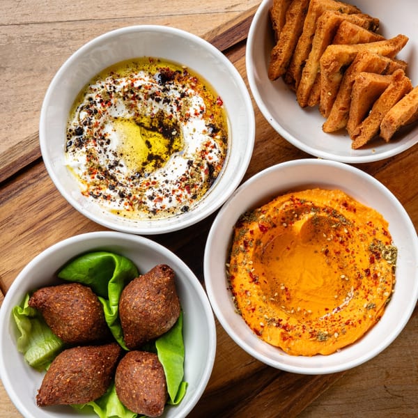 Four bowls of Middle Eastern appetizers, including kibbeh, hummus, labneh, and fried bread, on a wooden surface.