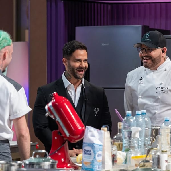 Three men, including a chef in a Bachour hat, smiling in a kitchen with a red mixer.