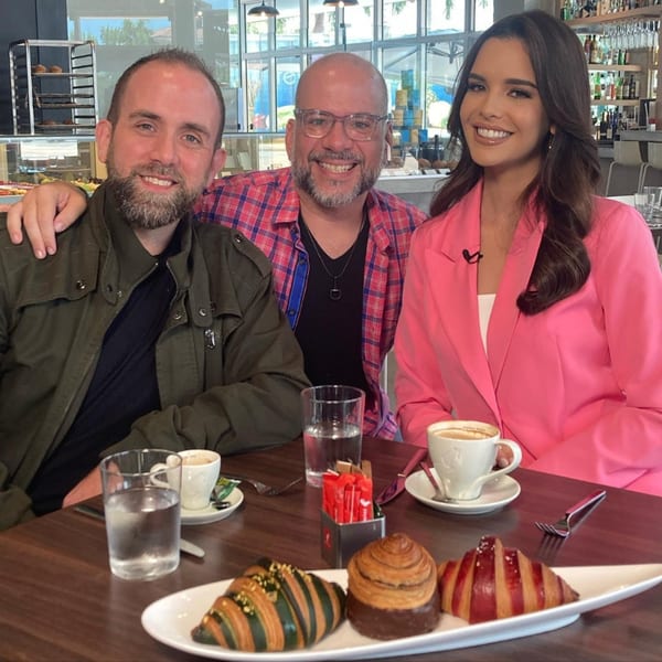 Three smiling people at Bachour bakery, with colorful croissants and coffee on the table.