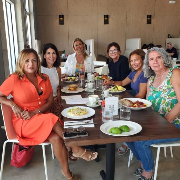 Six women smiling at a table with various breakfast and brunch dishes at Bachour bakery.