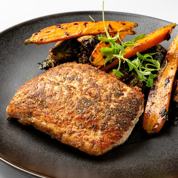 Seared salmon with roasted carrots, Brussels sprouts, and microgreens on a dark plate.
