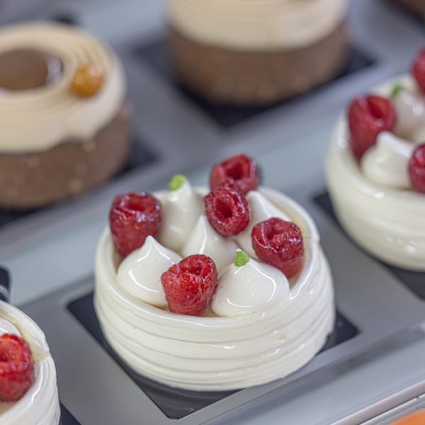 Close-up of a white Bachour pastry topped with fresh raspberries and cream swirls.