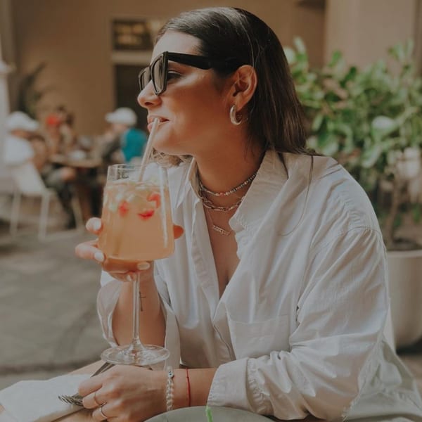 Woman in sunglasses sips a pink drink with strawberries through a straw at Bachour.