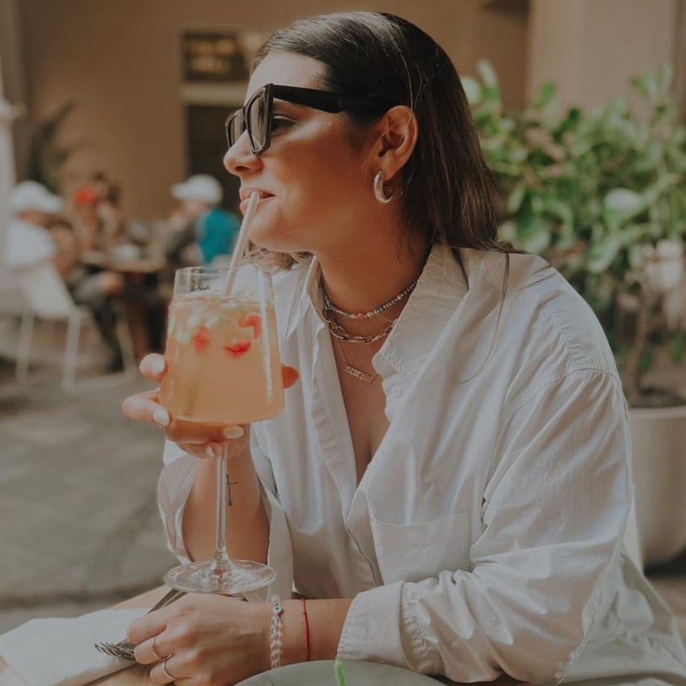 Woman in sunglasses sips a pink drink with strawberries through a straw at Bachour.