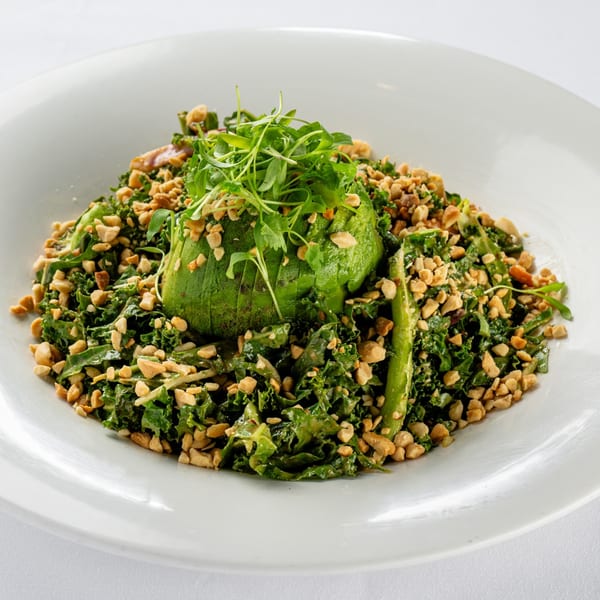 A vibrant green kale salad with sliced avocado, topped with microgreens and chopped peanuts.