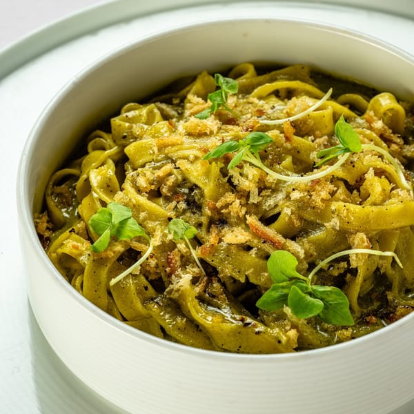 Close-up of green pasta with breadcrumbs and fresh herbs in a white bowl.