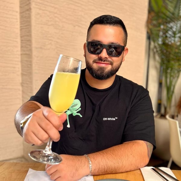 A man in sunglasses and a black shirt holds up a glass of mimosa at Bachour.